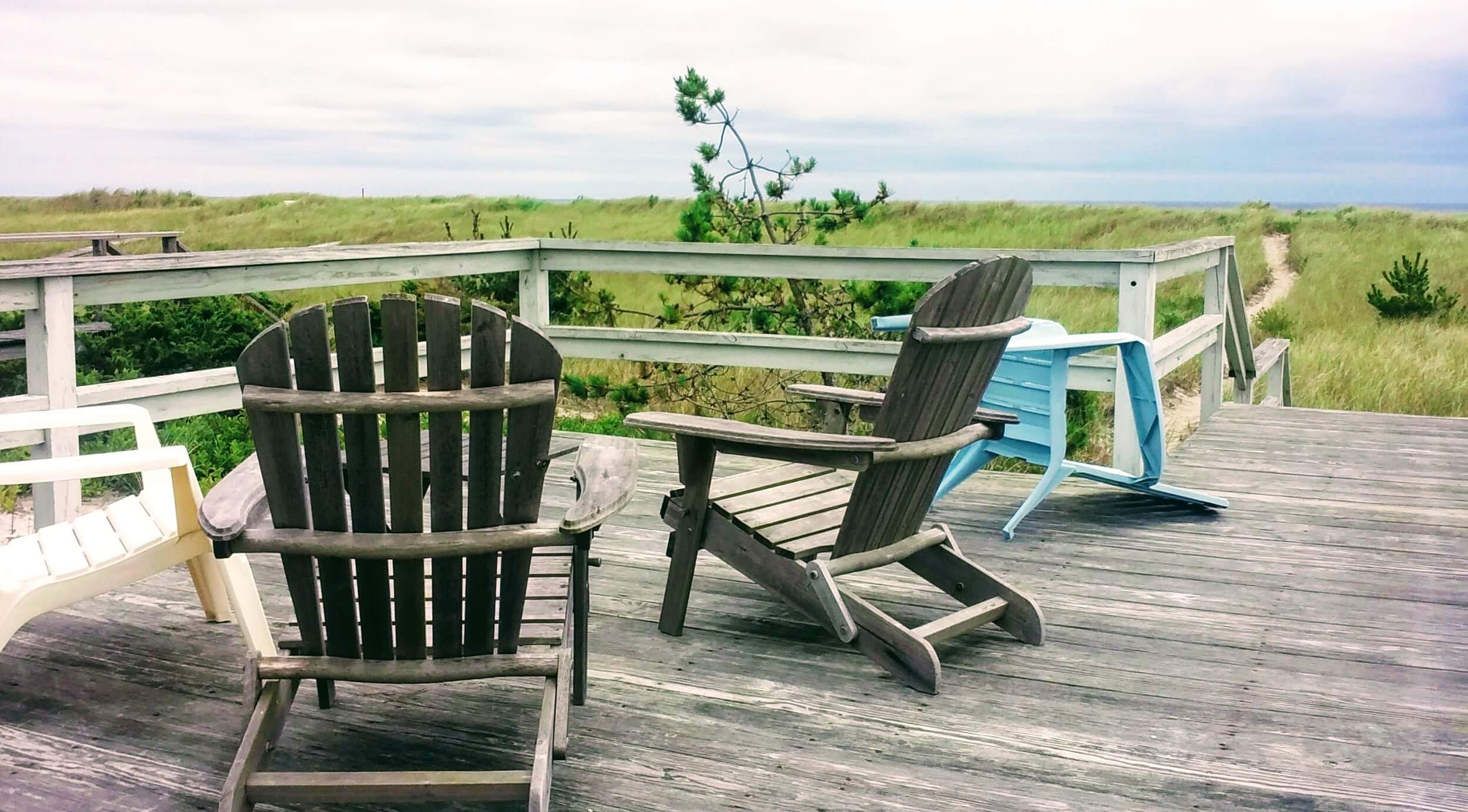 Beach grass and cloudy skies with forgotten Adirondack chairs turned on their sides